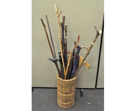 A wicker stick stand containing a shooting stick, umbrellas, walking sticks and other items