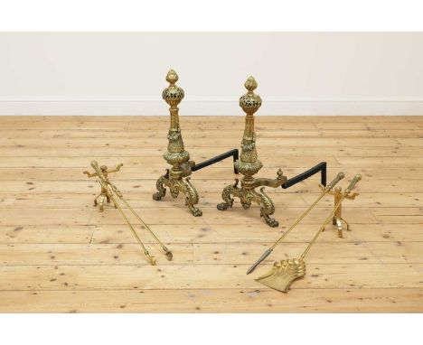 A pair of neoclassical brass firedogs,late 19th century, each with embossed floral and foliate decoration, surmounted by an a