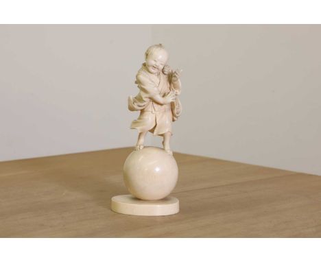 A Japanese carved ivory figure of a child,Meiji period, (late 19th century) standing on a sphere, on a wooden stand, incised 