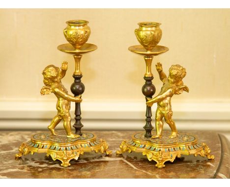 A pair of French ormolu and champleve enamel candle holders, circa 1890-1910, each modelled as a cherub standing beside a kno
