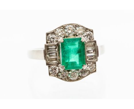 An emerald and diamond platinum dress ring, the central claw set emerald cut measuring approx. 8mm x 6mm x 4.9mm, within a bo