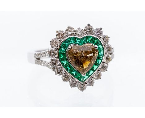 A diamond and emerald heart shaped 18ct white gold ring, comprising a heart cut champagne diamond claw set to the centre with