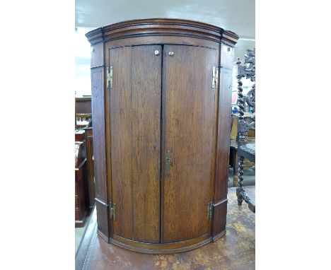 A George III style oak bow-front wall hanging corner cupboard