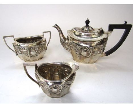 Edwardian three piece tea service comprising tea pot, milk jug and sucrier, faceted and embossed with scrolled cartouche and 