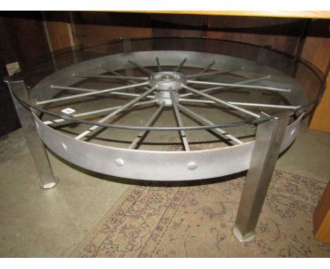 A vintage agricultural implement wheel raised on later polished steel supports with inset plate glass top, 125 cm diameter x 