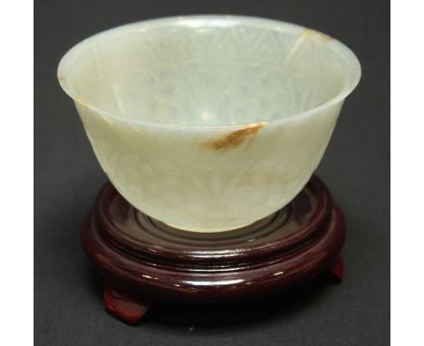 A 20th century Chinese carved pale jade bowl, the exterior carved with flower and geometric bands, on a turned wooden stand. 