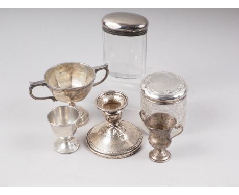 Two silver mounted dressing toilet jars, two miniature silver trophy cups, a silver egg cup and a squat silver candlestick, 7