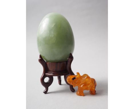 A turned jade egg, 2 1/2" high, on hardwood stand, and an amber carved elephant, 1" high 