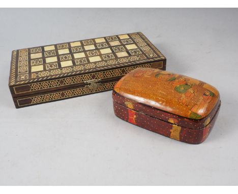 A parquetry and mother-of-pearl chess and backgammon board with carved soapstone pieces, a papier-mache box with black and wh