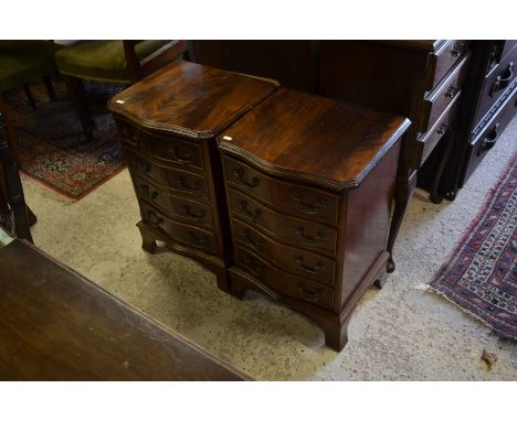 A pair of reproduction mahogany serpentine front bedside chests each having four drawers with brass handles, raised on bracke