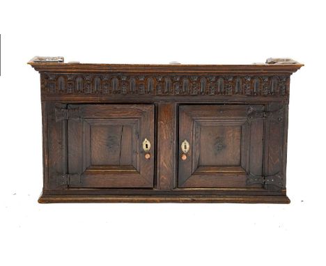 A 17th Century Joined Oak Wall-Mounted Cupboard, the bold cornice above a nulled frieze and two moulded cupboard doors with i
