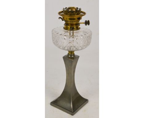 An early 20th century pewter oil lamp with clear cut glass reservoir and brass mountings above a tapering stem to square base