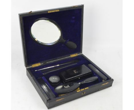 A leather cased ebony travelling set comprising rectangular trinket box, hand mirror, hairbrush, a pair of clothes brushes, g