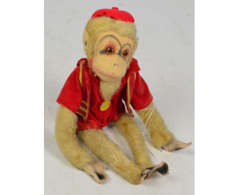A vintage yes/no monkey with felt face and ears and bendy arms and legs, dressed in a red shorts outfit with red cap, tail op