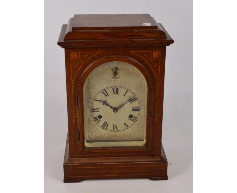 An early 20th century oak and inlaid cased chiming eight day mantel clock, the arched silvered engraved face with circular di