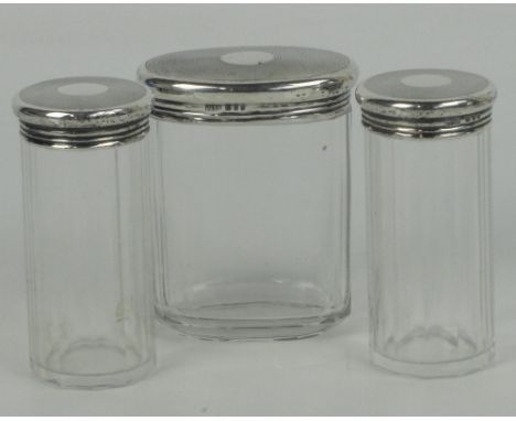 Three George VI hallmarked silver topped fluted glass dressing table jars, two cylindrical and one oval, with engine turned d