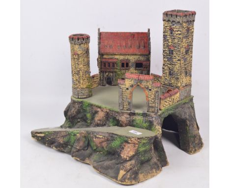A board and papier-mâché model train tunnel with a house/castle with towers and entrance gate above and a sloping road to one