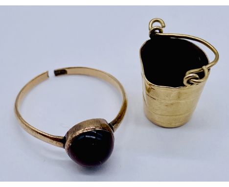 An 18ct gold ring set with a cabochon garnet (A/F, total weight 1.6g) along with a 9ct gold charm in the form of a bucket (we