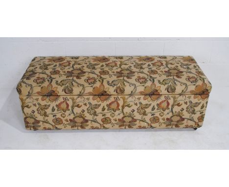 An antique ottoman upholstered in a floral printed tapestry material, on castors, 135 cm wide, 55 cm deep, 44 cm high