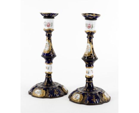 
	
		A pair of 19th century enamel candlesticks decorated with Watteauesque panels within gilt borders and reserved on a blue