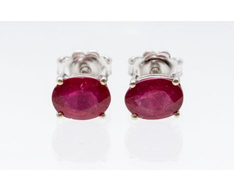 A pair of ruby and silver stud earrings, claw set with oval rubies approx 5 x 7mm, treated rubies,  post and scroll pierced f
