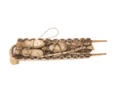 An Inuit whalebone model of a sled:  laden with seals, guns, cartridge bag and shot flask,  12.5cm long.