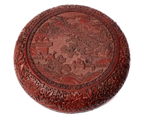 A Chinese carved cinnabar lacquer box and cover: of circular form, carved to the centre with a mountainous river landscape wi