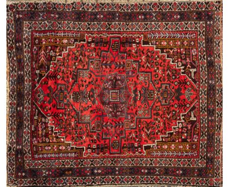 A Quashgai carpet:, the brick red stepped and pointed lozenge field with a central pastel blue geometric pole medallion, all 