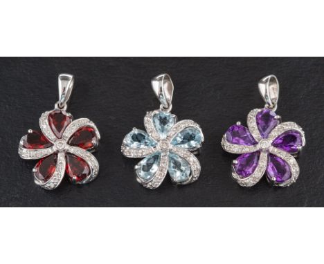 Three 18ct white gold pendants of stylised flowerhead design,: set with garnets, amethysts and light blue topaz, accented wit