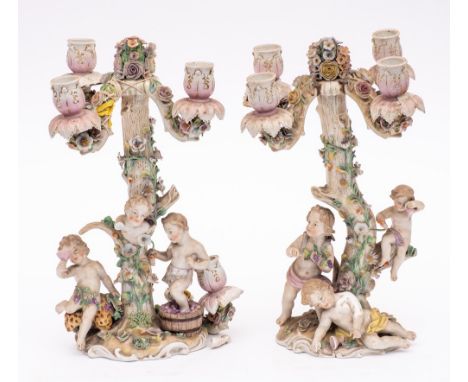 A pair of Dresden porcelain figural four-branch candelabra: modelled as bacchanalian putti around a tree trunk, the whole app