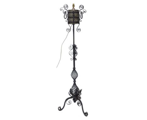A wrought iron standard lamp, with brass embossed reservoir, the column decorated with scrolls and twisted balusters, the tri