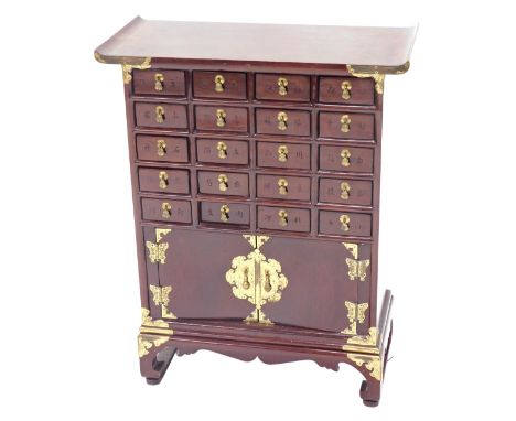 A Chinese small hardwood cabinet, with brass mounts and arrangement of twenty drawers and two doors, each with elaborate butt