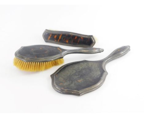 A George V tortoiseshell and silver mounted three piece dressing table set, comprising hand mirror, hairbrush and a clothes b