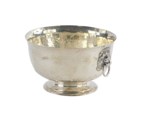 A George V silver two handled bowl, with hammered decoration, the two handles cast with lion heads, on a pedestal base, Londo
