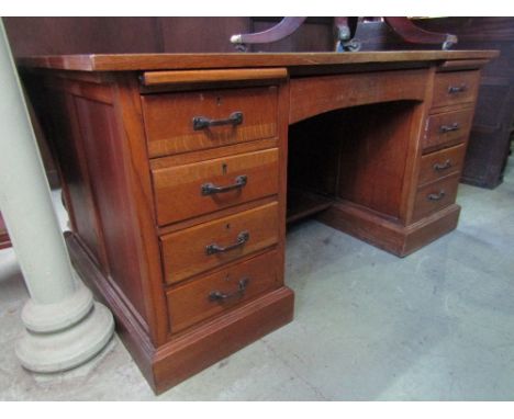 A medium oak kneehole twin pedestal desk with inset faux leather top over an arrangement of nine drawers with brushing slides