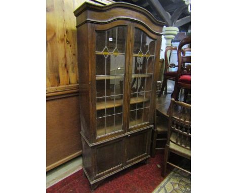An early 20th century oak bookcase, freestanding and enclosed by two pairs of panelled doors, the upper with leaded light doo