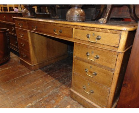 A Victorian pale oak pedestal writing desk fitted with nine frieze drawers and brass swan neck handles, with inset leather to