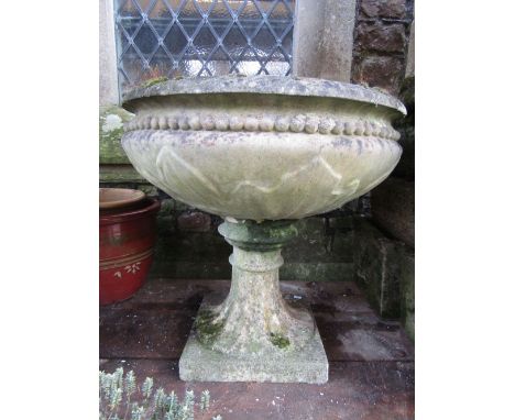 A weathered cast composition stone garden planter, the circular shallow bowl with bead and leaf detail raised on a fluted ped