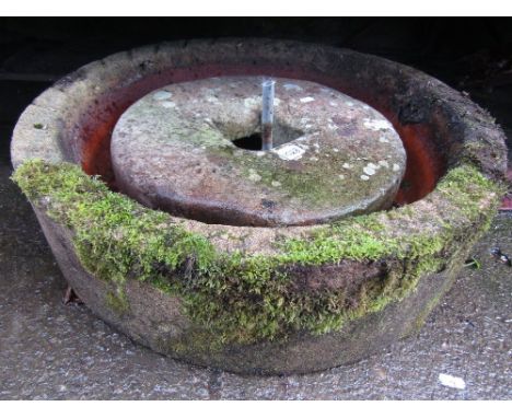 A small weathered natural stone mill grinding wheel together with a weathered shallow circular planter/water feature, and a c