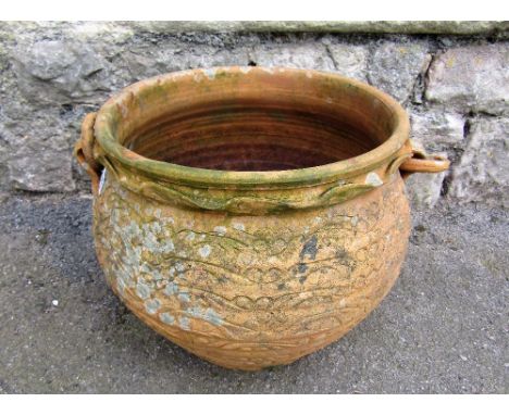 A weathered terracotta planter with loose ring handles and incised foliate detail