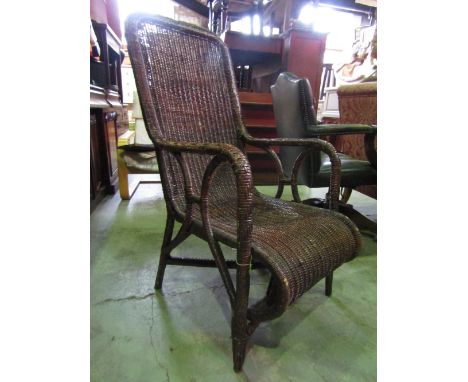 A vintage wicker armchair with stained finish, drop arms and scrolled seat