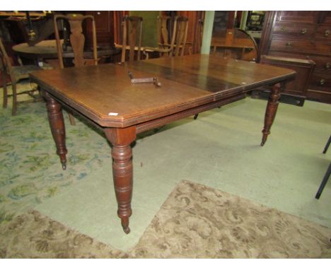 An Edwardian oak wind out extending dining table of rectangular form with moulded outline, canted corners and two additional 