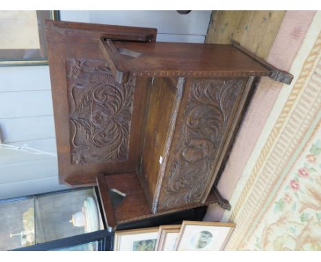 A carved oak monk's bench, the hinged top/back carved with dragons over a lidded seat carved with a mask and scrolls, 91cm wi