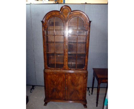 A Queen Anne standing display cabinet, having tri-arched design to top, with upper glazed section revealing three interior sh