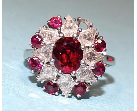 A 1970's ruby and diamond cluster ring, the central oval ruby within a surround of eight fancy-cut diamonds and seven (one mi