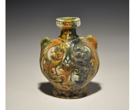 An undated archaistic glazed ceramic vessel in shades of green, olive and cream, floral detail to the body with lugs to the s