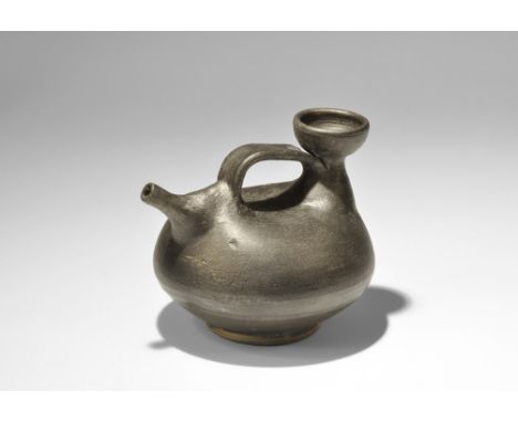 4th century BC. A ceramic blackware pouring vessel with discoid body, incised lines to the shoulder, narrow funicular spout, 