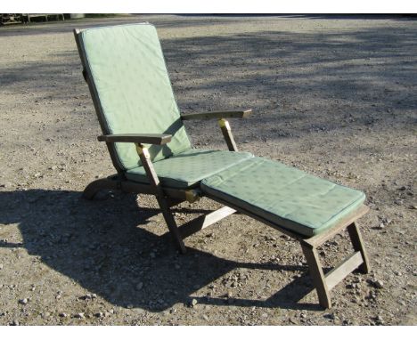 A weathered teak folding steamer type chair with slatted, seat back and footrest, complete with loose cushion