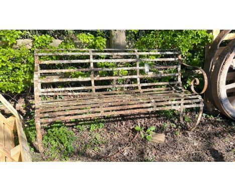 An antique sprung iron strap work bench with scrolling arm rests, with remnants of original painted finish, with lichen cover