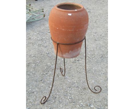 A weathered terracotta oviform  jar set/raised on a simple iron stand with scrolled supports, 82 cm (full height)